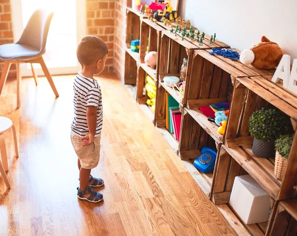 漂亮的蹒跚学步的男孩站在幼儿园 手里拿着很多玩具 — 图库照片