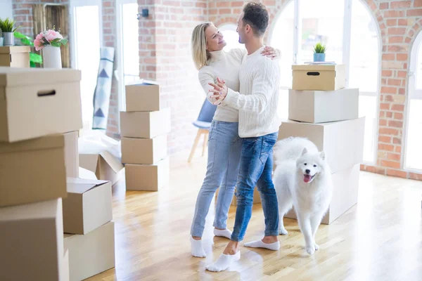 Young beautiful couple with dog dancing at new home around cardboard boxes