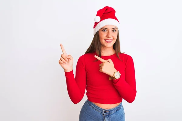若いです美しいです女の子身に着けていますクリスマスサンタ帽子立って上の隔離された白い背景笑顔と見てカメラを指しています二つの手と指で側面へ — ストック写真