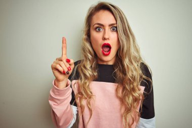 Eşofman üstü giyen genç ve çekici bir kadın izole edilmiş beyaz arka plan üzerinde durup başarılı bir fikir işaret ediyor. Heyecanlı ve mutlu. Bir numara..