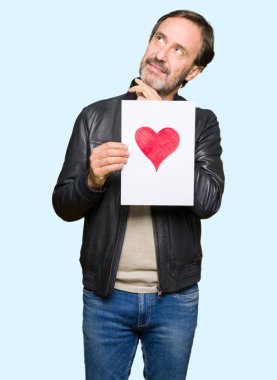 Kırmızı kalp ciddi bir yüz düşünce hakkında soru, çok karışık bir fikir ile kağıt tutan yakışıklı orta yaş erkek