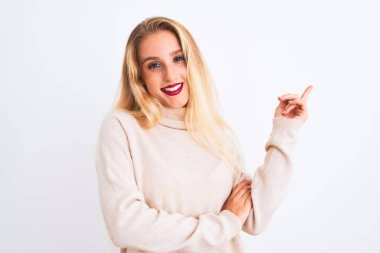 Balıkçı yaka kazak giyen genç ve güzel bir kadın izole edilmiş beyaz arka plan üzerinde duruyor. Yüzünde kocaman bir gülümseme, eli ve parmağı kameraya bakıyor..