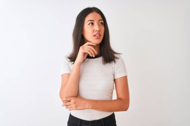İzole edilmiş beyaz arka planda el pençe divan duran ve soru soran, düşünceli bir tişört giyen genç, güzel Çinli kadın. Düşünceli bir yüzle gülümsüyor. Şüphe kavramı.