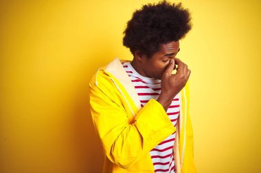 Siyah saçlı Afrikalı bir adam izole edilmiş sarı arka planda dikilmiş yorgun burnu ve gözleri ovuşturarak yorgunluk ve baş ağrısı hissediyordu. Stres ve hüsran kavramı.