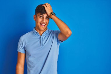 İzole edilmiş mavi arka planda dikilen sıradan polo giyen genç Hintli adam hata sonucu el ele tutuşarak şaşırdı. Hatayı hatırla. Unuttum, kötü hafıza konsepti.