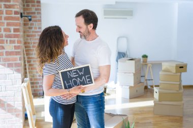 Orta yaş Senior çift yeni bir eve hareket, yeni bir ev metin ile bir tahta tutan Apartmant aşık mutlu gülümseyen