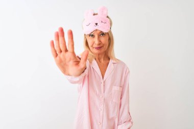 İzole edilmiş beyaz arka plan üzerinde uyku maskesi ve pijama giyen orta yaşlı kadın avucunun içi gibi şarkı söylemeyi kesiyor. Yüzünde olumsuz ve ciddi bir jest olan uyarı ifadesi.