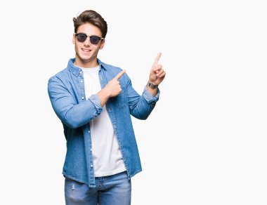 Yakışıklı delikanlı gülümseyen ve iki elleri ve parmakları ile tarafına işaret kamera bakarak izole arka plan üzerinde güneş gözlüğü takıyor.