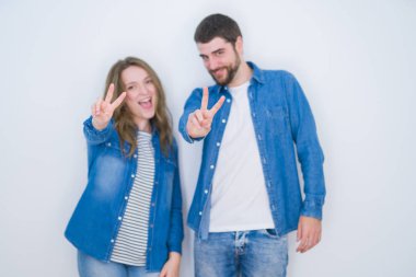 İzole edilmiş beyaz arka planda yan yana duran genç ve güzel bir çift kameraya bakıp zafer işareti yapıyor. İki numara..