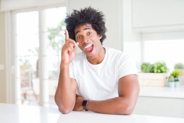 Sıradan beyaz tişörtler giyen genç Afro-Amerikan bir adam evde oturmuş başarılı bir fikri işaret ediyor. Heyecanlı ve mutlu. Bir numara..