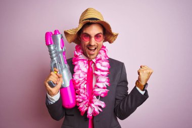 Su tabancası takan genç iş adamı Hawai lei şapka gözlükleriyle pembe arka planda gururla bağırıyor ve zaferi ve başarıyı kutluyor.