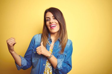 Sarı arka planda duran genç ve güzel bir kadın. Arka tarafı işaret ediyor. El ve baş parmakları havada, kendine güvenen.