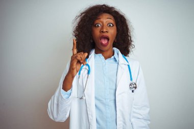 İzole edilmiş beyaz arka plan üzerinde steteskop takan genç Afro-Amerikan doktor kadın başarılı bir fikri işaret ediyor. Heyecanlı ve mutlu. Bir numara..