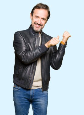 Siyah deri giyen orta yaş yakışıklı adam kendinden emin gülümseyen işaretleme için arkasından el ve başparmak yukarıya, ceket