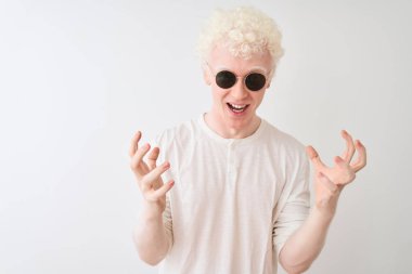 Genç albino, tişört ve güneş gözlüğü takan, çılgın ve hayret verici başarısını kutlayan, kollarını kaldırmış ve gözleri açık, heyecanlı bir şekilde çığlık atan, izole edilmiş beyaz bir arka plan. Kazanan konsept