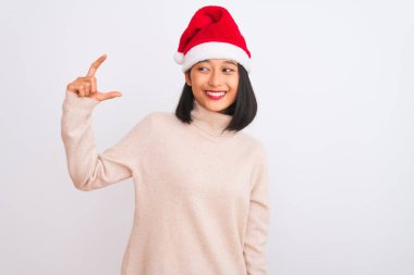 Noel Baba şapkası takan genç, güzel Çinli bir kadın izole edilmiş beyaz arka planda gülümseyen ve kendine güvenen el hareketleriyle küçük boy işareti yapan parmaklarıyla ve kamerasıyla. Ölçü kavramı.