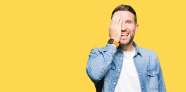 Yakışıklı adam mavi gözleri ve denim ceket kapsayan bir gözün elle kendine güvenen gülümseme ile yüz ve sürpriz duygu üzerinde giyen sakal.