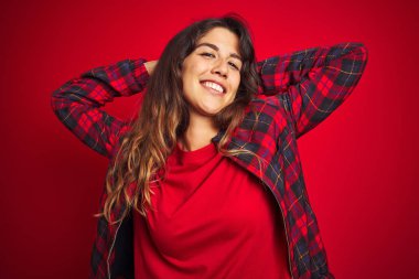 Kırmızı izole edilmiş arka plan üzerinde duran sıradan bir ceket giyen genç ve güzel bir kadın. Baş parmaklarını yukarı aşağı hareket ettiriyor. Anlaşmazlık ve anlaşma ifadesi. Çılgın çatışma