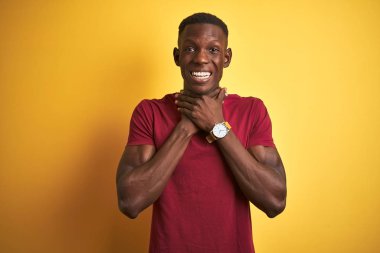 Kırmızı tişört giyen genç Afro-Amerikalı adam izole edilmiş sarı arka planda durup bağırıyor ve boğuluyor çünkü acı verici bir boğulma. Sağlık problemi. Boğulma ve intihar konsepti.