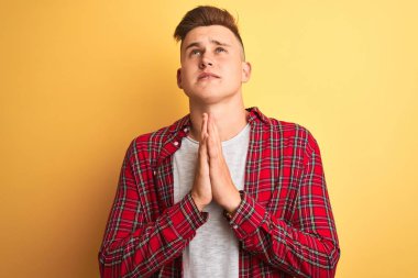 Sarı arka plan üzerinde duran sıradan tişörtlü genç yakışıklı adam elleri bağlı yalvarıyor ve dua ediyor. Yüzünde umut ifadesi var. Çok duygusal ve endişeli. Af diliyor. Din kavramı.