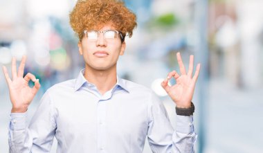 Genç yakışıklı iş adamı ile gözlüklü afro rahatla ve gülümseyen gözlerle kapalı parmak jestle meditasyon yapıyor. Yoga kavramı.