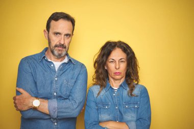 Güzel orta yaşlı çift, izole edilmiş sarı arka plan üzerinde birlikte duruyorlar şüpheci ve gergin, yüzlerinde çapraz kollarla onaylamayan ifade. Negatif kişi.