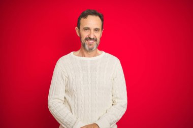 Yakışıklı, orta yaşlı, gri saçlı, izole edilmiş kırmızı arka planı olan, elleri çapraz parmaklı, gevşemiş ve neşeli gülümseyen bir adam. Başarı ve iyimser