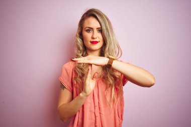 Pembe izole edilmiş arka planda duran tişört giyen genç ve güzel bir kadın. Elleriyle jest yapıyor, hayal kırıklığına uğramış ve ciddi bir yüz ifadesi takınıyor.