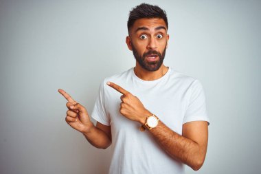 İzole edilmiş beyaz arka plan üzerinde duran genç Hintli adam iki eliyle endişeli ve endişeli bir ifadeye işaret ediyor.