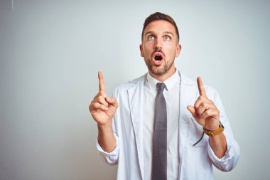 Soyutlanmış arka planda beyaz kürk giyen yakışıklı genç doktor şaşırmış ve şaşırmış bir şekilde yukarı bakıp parmaklarını göstermiş ve kollarını kaldırmıştı..