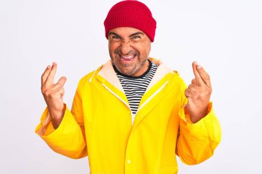 Yağmurluk giyen ve yünlü şapkalı orta yaşlı bir adam izole edilmiş beyaz arka planda durup umut ve gözlerin kapalı gülümseyerek el sallıyor. Şans ve batıl inanç..