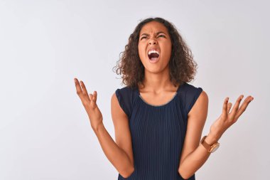 Mavi elbise giyen genç Brezilyalı kadın izole edilmiş beyaz arka planda çılgın ve sinirli bir şekilde duruyor ve agresif bir ifadeyle bağırıyor ve kollarını kaldırıyor. Hayal kırıklığı konsepti.