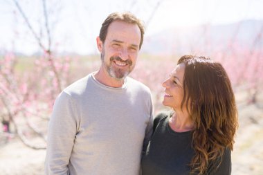 Baharın güneşli bir gününde pembe yaprakları ile şeftali ağaçlarının romantik bahçesinde aşık gülümseyen güzel orta yaş yaşlı çift