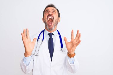 Orta yaşlı doktor ceketli ve steteskop takmış beyaz arka planda çılgın deli bağırıyor ve agresif bir ifade ve kollarla bağırıyor. Hayal kırıklığı konsepti.