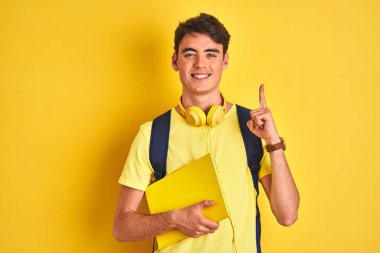 Kulaklık takan ve sırt çantalı genç bir çocuk izole edilmiş arka planda kitap okuyor. Bir fikir ya da soru işareti ile şaşırmış, mutlu yüzle bir numara.