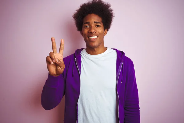 ピンクの背景に紫色のスウェットシャツを着た若いアフリカ系アメリカ人男性がピンクの背景を見せ 自信を持って幸せな笑顔で指の数2で指摘 — ストック写真