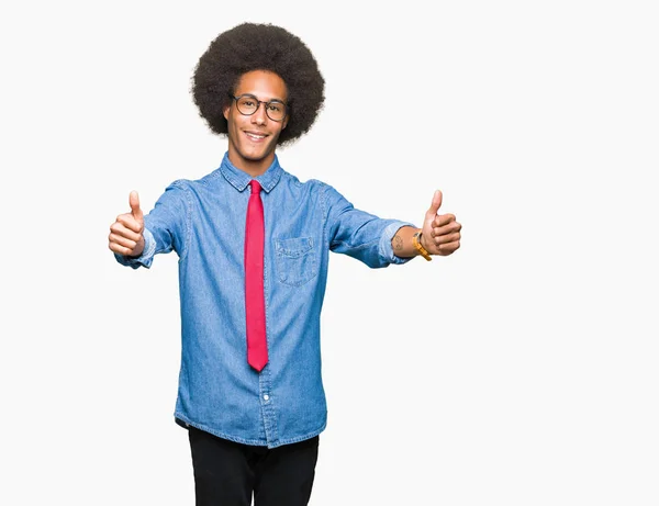 非洲青年商人与非洲头发戴眼镜和红色领带批准做积极的手势 竖起大拇指微笑 并为成功高兴 看着镜头 赢家的手势 — 图库照片