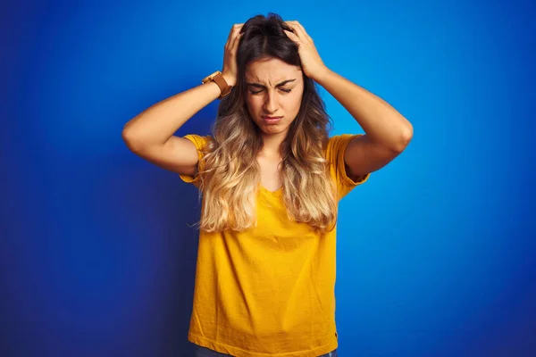 Young beautiful woman wearing yellow t-shirt over blue isolated background suffering from headache desperate and stressed because pain and migraine. Hands on head.