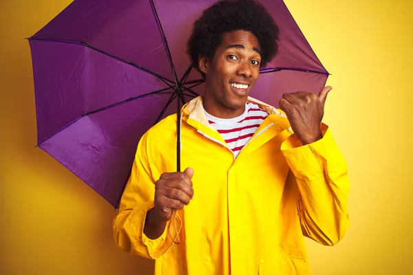 Афро Американец Дождевой Куртке Зонтике Стоящий Изолированном Желтом Фоне Указывая — стоковое фото