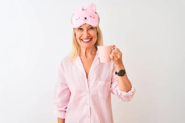 Middle age woman wearing sleep mask pajama drinking coffee over isolated white background with a happy face standing and smiling with a confident smile showing teeth