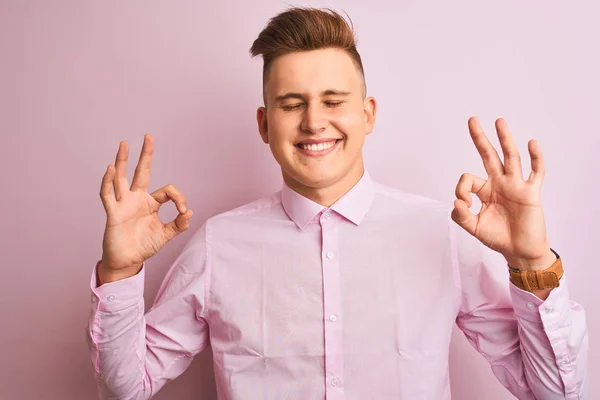 年轻英俊的商人穿着雅致的衬衫 站在孤立的粉色背景上放松 闭上双眼微笑 用手指做冥想动作 瑜伽概念 — 图库照片