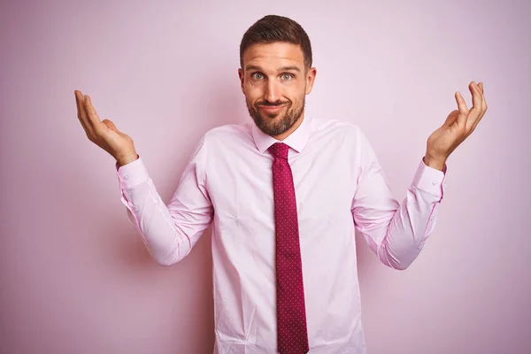 Business man wearing tie and elegant shirt over pink isolated background clueless and confused expression with arms and hands raised. Doubt concept.