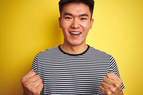 身穿条纹T恤的年轻的亚裔男子站在孤立的黄色背景上自豪地尖叫着 为胜利和成功欢呼着 为自己的情绪欢呼着 — 图库照片