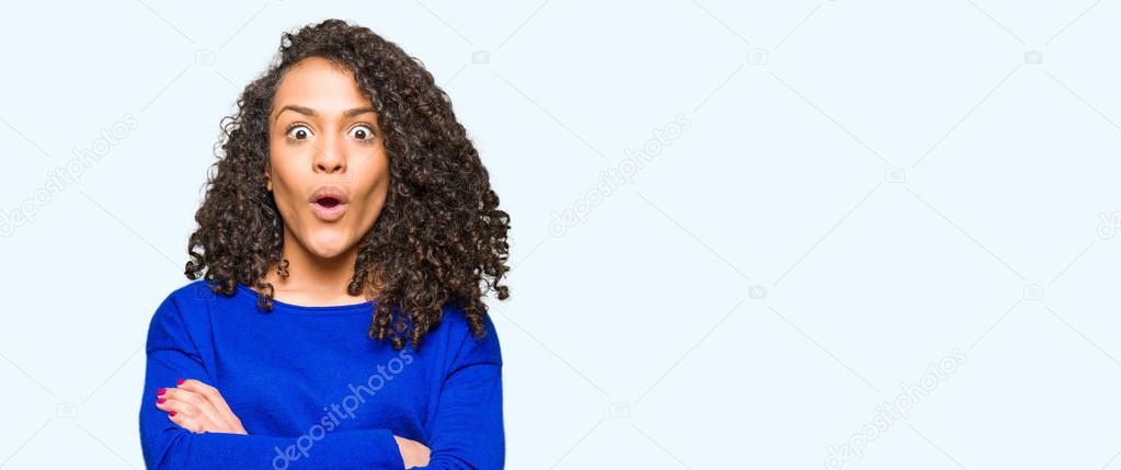 Young beautiful woman with curly hair wearing winter sweater afraid and shocked with surprise expression, fear and excited face.