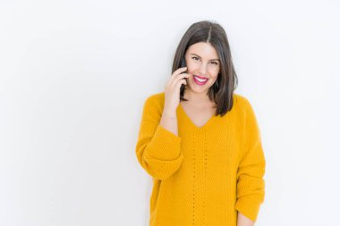 Güzel esmer genç kadın kendine güvenen arama Smartphone kullanarak rahat sarı kazak giyen izole beyaz arka plan üzerinde gülümseyen