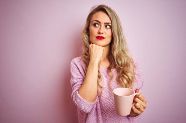 Süveter giyen, pembe izole edilmiş arka planda bir fincan kahve içen genç ve güzel bir kadın.