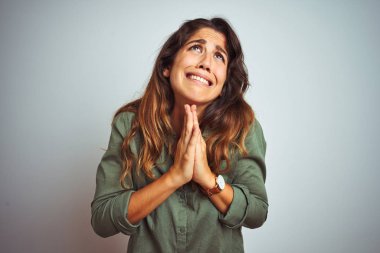 Gri arka plan üzerinde duran yeşil tişörtlü genç ve güzel bir kadın elleri bağlı yalvarıyor ve dua ediyor. Yüzünde umut ifadesi var. Çok duygusal ve endişeli. Af diliyor. Din kavramı.