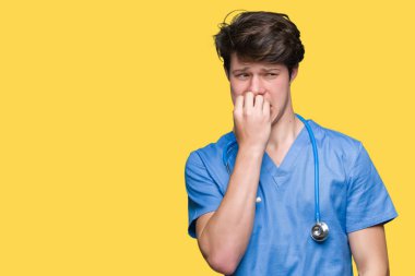 Stresli ve gergin elle çivi ısırma ağzına bakarak izole arka plan üzerinde tıbbi üniforma giyen genç doktor. Anksiyete sorunu.