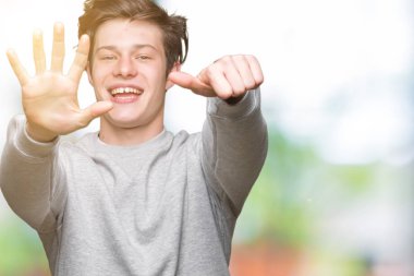 Gösterilen arka plan üzerinde sweatshirt giyen genç yakışıklı sportif adam izole ve parmakları ile işaret kendinden emin ve mutlu gülümseyerek süre 6 numara.