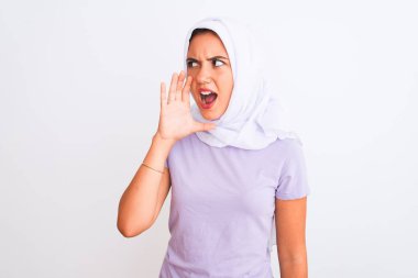 Genç, güzel, tesettürlü Arap bir kız izole edilmiş beyaz arka planda durup el ele tutuşarak bağırıyor ve bağırıyor. İletişim konsepti.